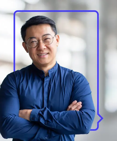 A smiling man in navy shirt and glasses standing with arms crossed, framed by a purple speech bubble outline over a blurred office background